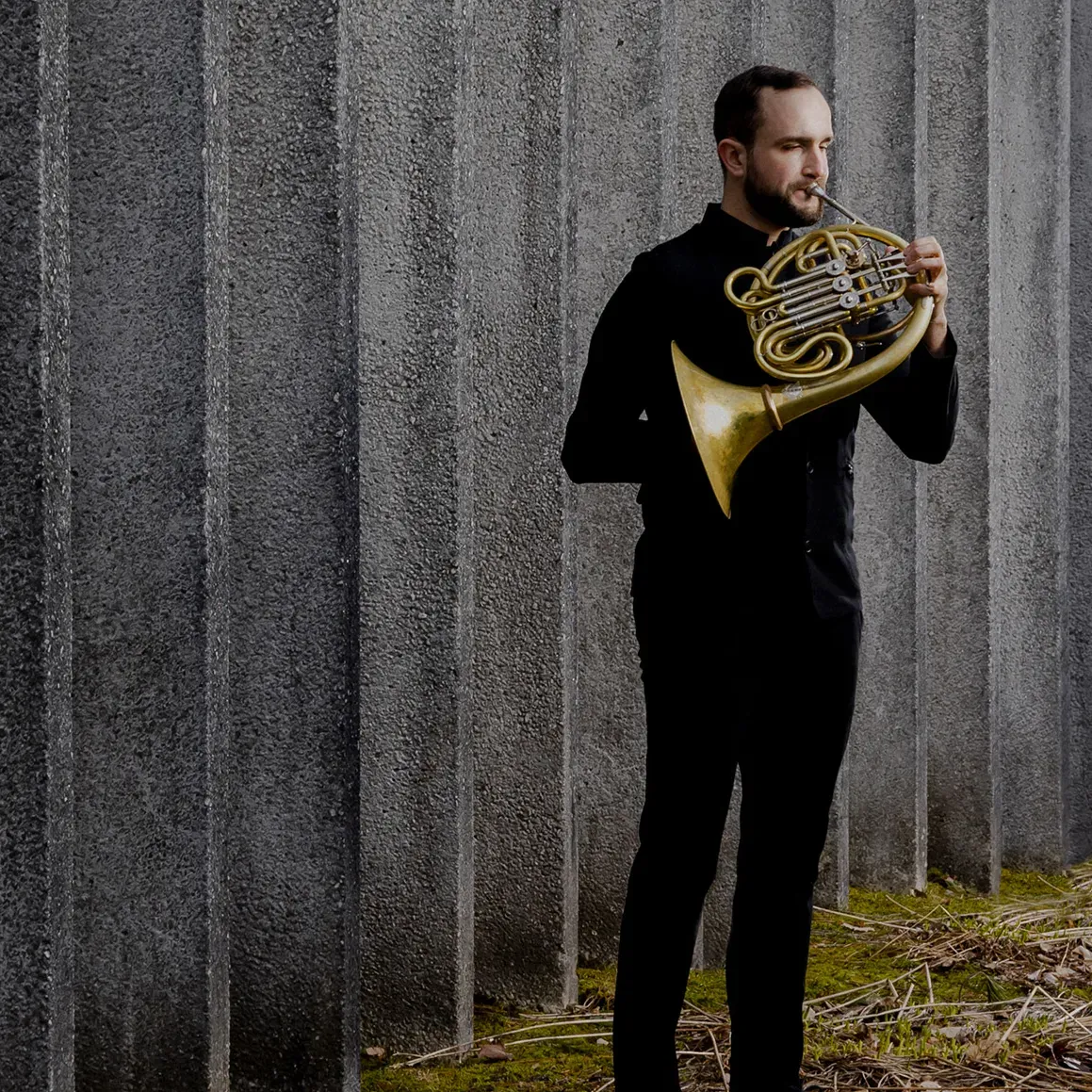 Photo of Gabriel Trottier playing the horn in front of a cement wall